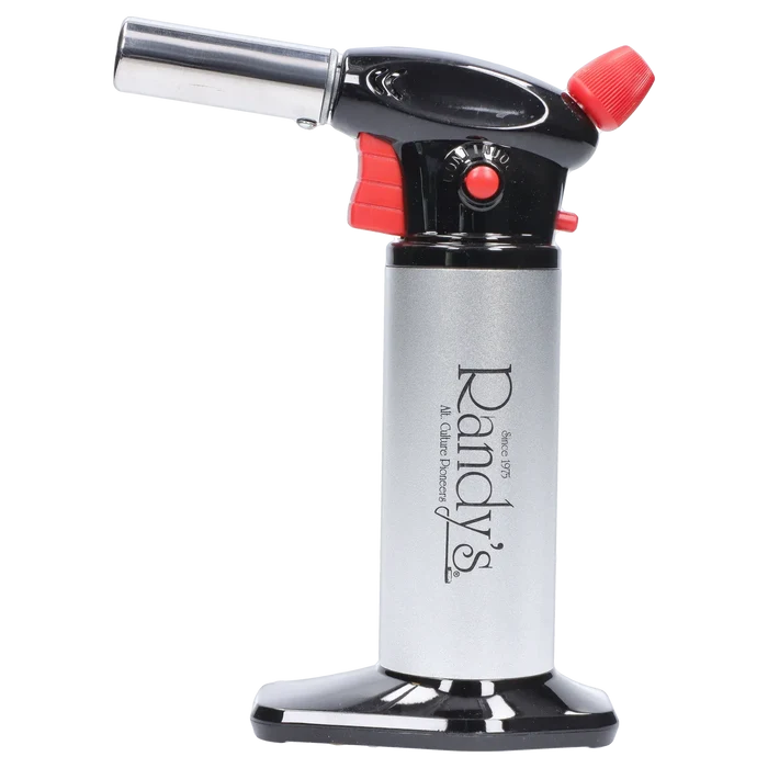 Side profile of Randy's Fahrenheit Butane Torch - Silver showing its chrome nozzle, black and red trigger head, and silver cylindrical body on a reflective black base